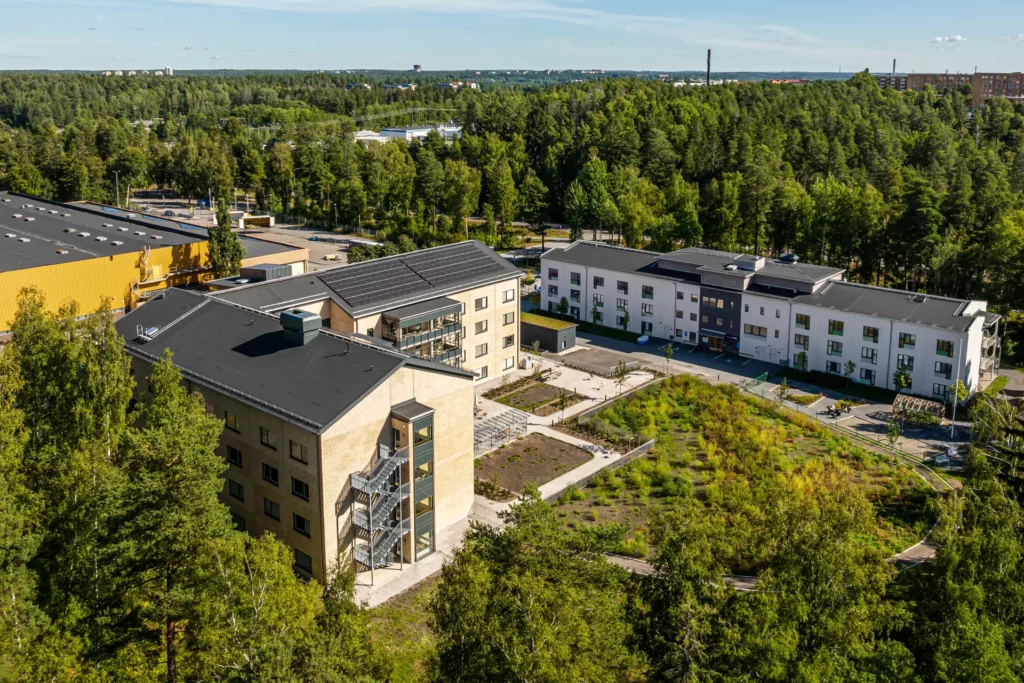 Flygfoto snett ovanifrån som visar boendet och mycket grön skog runtomkring.