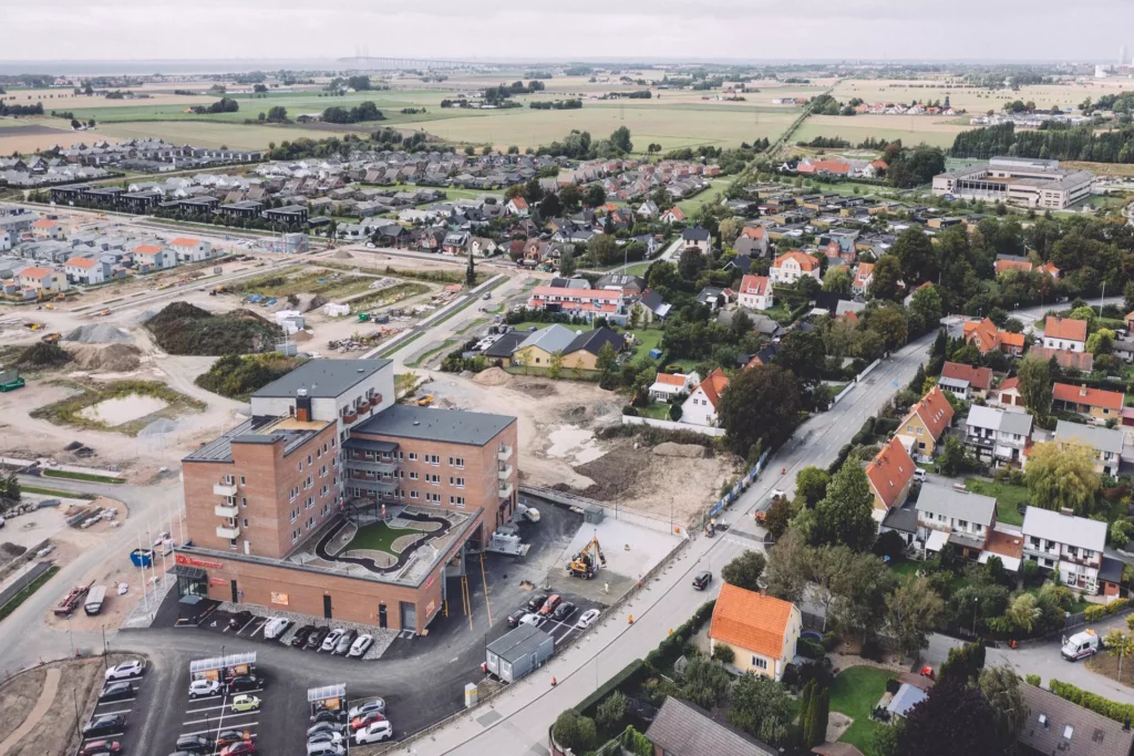 Flygfoto på byggnaden och parkeringen samt en del av området runt omkring boendet, med villor.