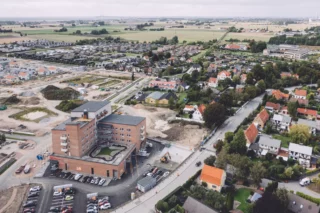 Flygfoto på byggnaden och parkeringen samt en del av området runt omkring boendet, med villor.