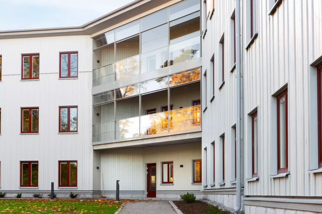 Äldreboendet HJohannas trädgård fotat från boendes baksida, som vetter mot äppellunden. I miten av bilden syns våningsplanens gemensamma balkonger som är inglasade. Fasasen är i vitt och fönstrens foder är bruna.
