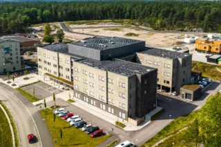 Södra Källtorps äldreboende i Västerås med fyra våningar. Boendet är i grå puts med grönområden runt om.