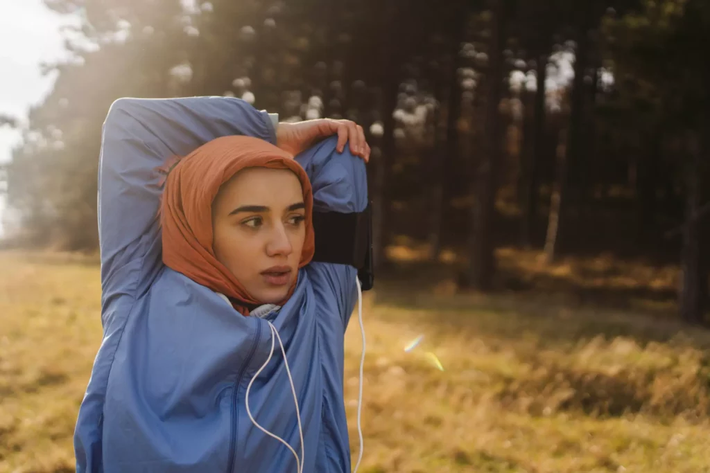 En ung tjej med blå träningskläder, orange sjal har precis avslutat sin löprunda en solig höstdag och stretchar.