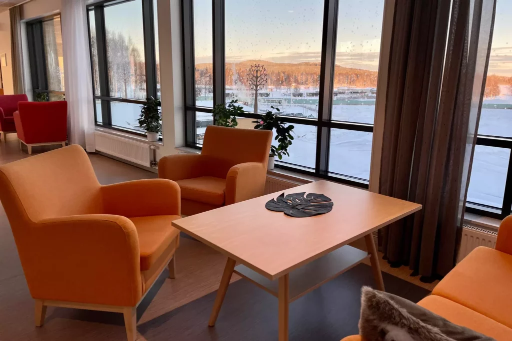 Trivsamt äldreboende i Boden, Björknäsgården, bilden visar en loungegrupp med en orange soffa och två fotöljer med en vacker vy utanför fönstren