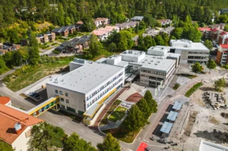 Flygfoto taget snett uppifrån över campusområdets vita huskroppar på tre våningar. Närområdet är lummigt med villor som främsta bebyggelse.