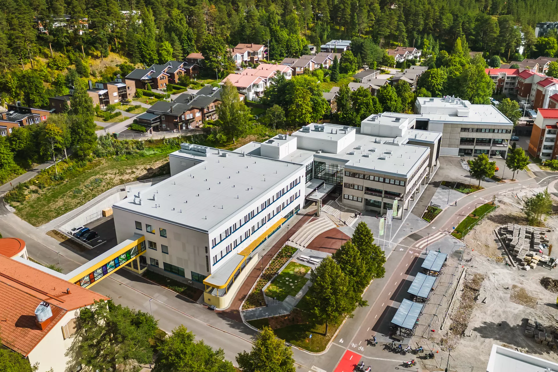 Flygfoto taget snett uppifrån över campusområdets vita huskroppar på tre våningar. Närområdet är lummigt med villor som främsta bebyggelse.