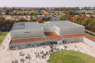 Visionsbild på Pilehallen från luften. Många människor syns strömma till hallen. I förgrunden en grön gräsmatta.
