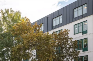 Vågen i Uppladns Väsby, förskola kombinerat med vård- och omsorgsboende i samma byggnad. Bilden visar en del av fasaden med ett träd på dess innergård i förgrunden
