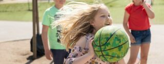 En ung flicka med långt ljust hår är på väg att kasta en grön basketboll.