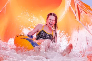 En flicka i tonåren kommer åkande i en orange rutschkana inomhus i Järfällabadet.