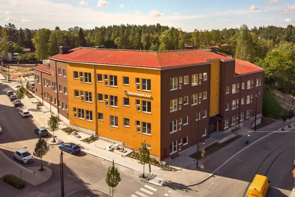 Nakterhusskolan i Haninge, en vacker skolbyggnad med fasad i en varm och jordnära färgskala med gula och bruna fasader. Sedumtak med växtlighet för att gynna den biologiska mångfalden.