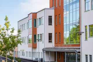 En nybyggd skola i orange och vit putsfasad. Vid entrén är hela mittenpartiet, alla tre våningar i glas.