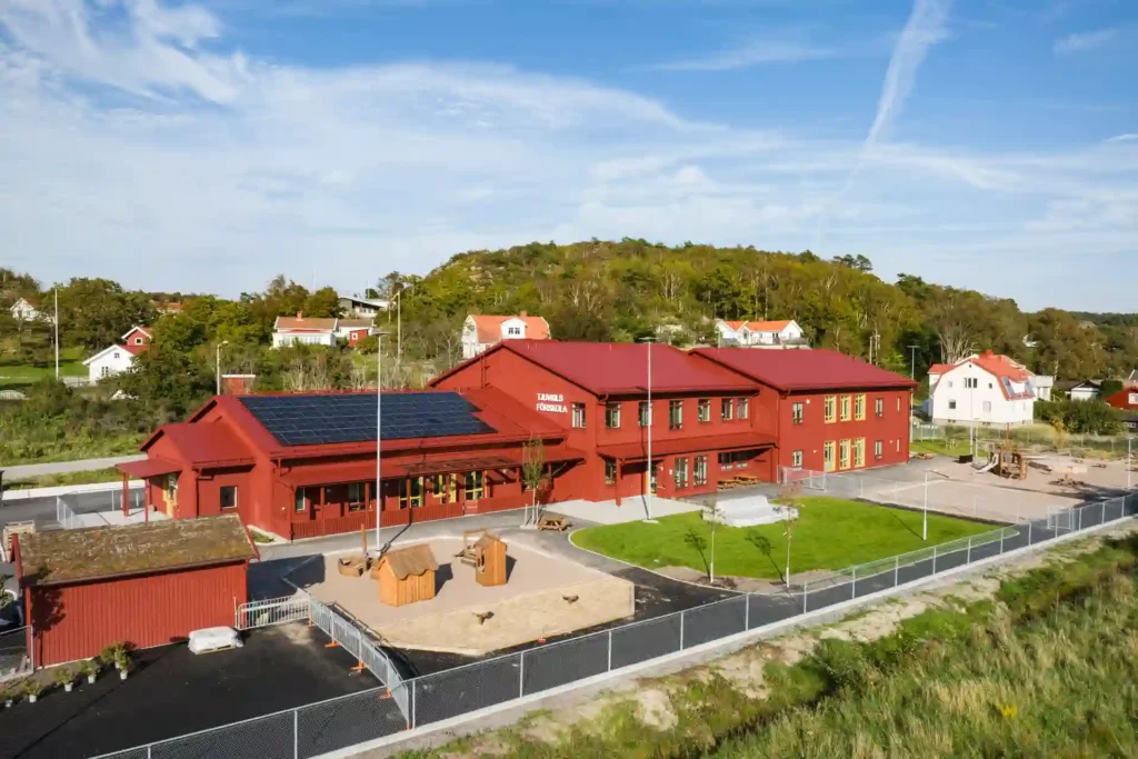 Tjuvkils förskola med fasad i rätt trä har två våningar i större delen av byggnaden. Solceller syns på taket till en del av byggnaden.