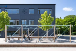 Bagartorpsskolan i Solna, en högstadieskola på tre våningar, grå fasad och i bilkden syns också en del av skolgården med en slags pergola där barnen kan sitta ner och vila och umgås under rasterna.