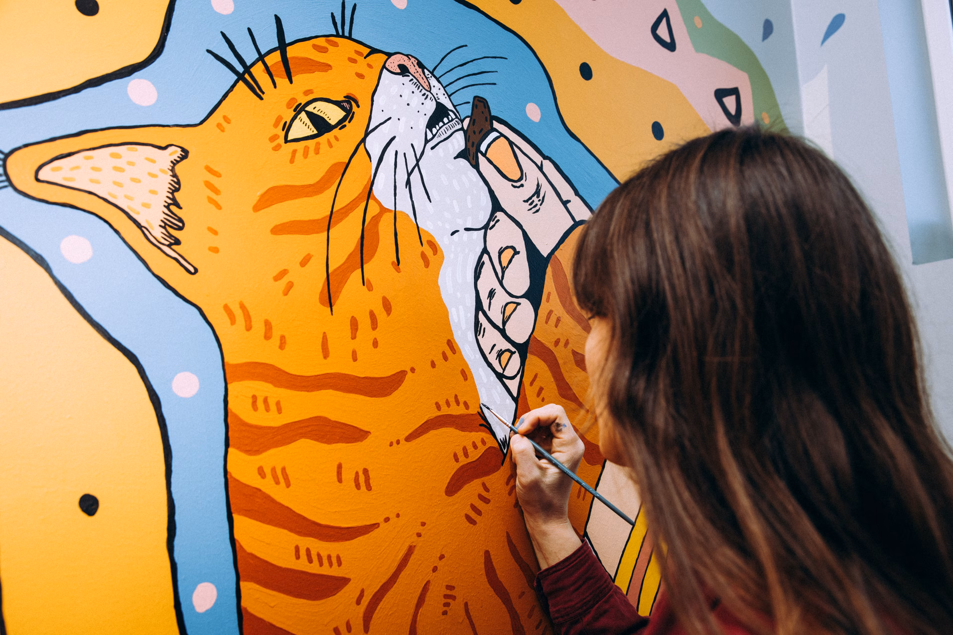 A woman painting a picture of a cat on a wall